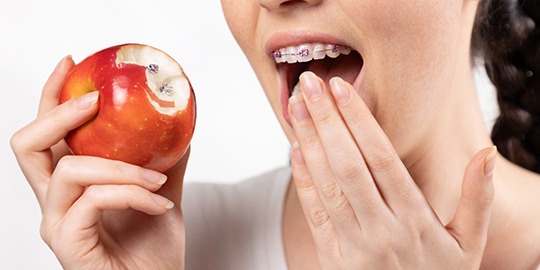 Woman touching broken braces with some in the apple she bit