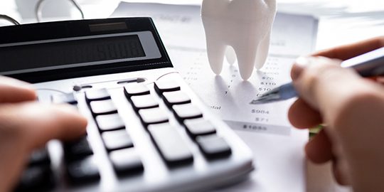 Hands holding pen and using calculator at desk with model tooth
