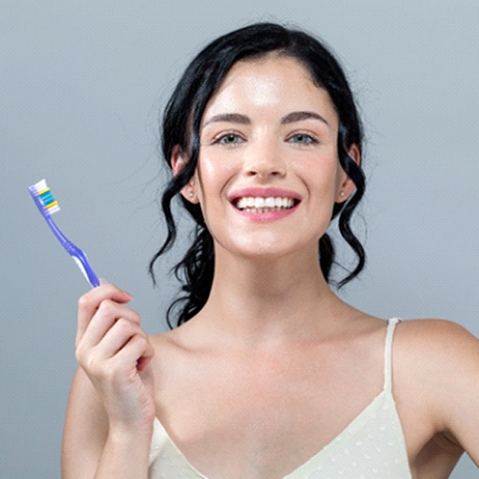 Woman holding toothbrush after Glo Science teeth whitening in Atlanta