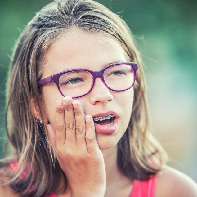 Teen girl with braces holding cheek before emergency orthodontic treatment