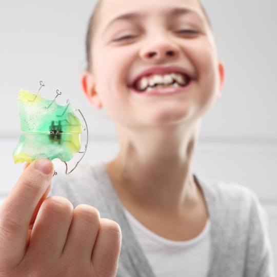 Young girl holding up a phase one orthodontics oral appliance
