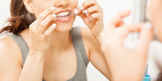 Closeup of woman using teeth whitening strip