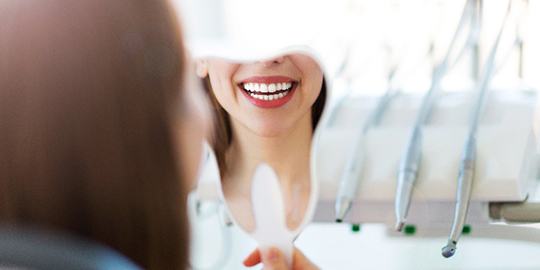 Woman smiling while looking into tooth-shaped mirror