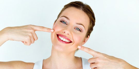 Woman smiling while pointing to her bright, white teeth