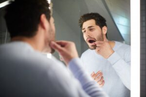 a man looking at his teeth in a bathroom mirror