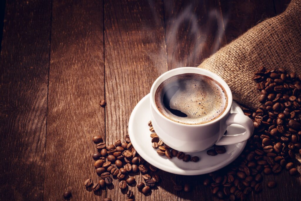 Cup of coffee with beans on wooden surface