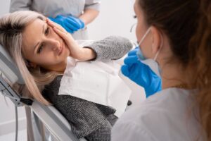 Woman in dentist's chair holding face in pain. 